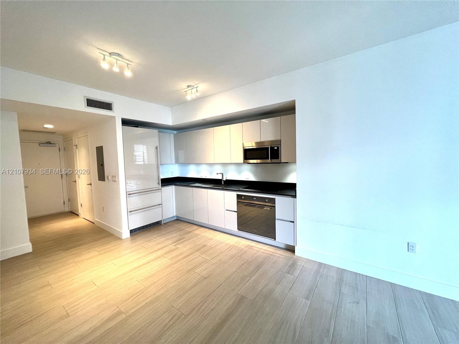 Modern kitchen featuring flat-panel cabinetry, a dark solid-surface countertop, an integrated refrigerator, stainless steel microwave, and wood-finish flooring