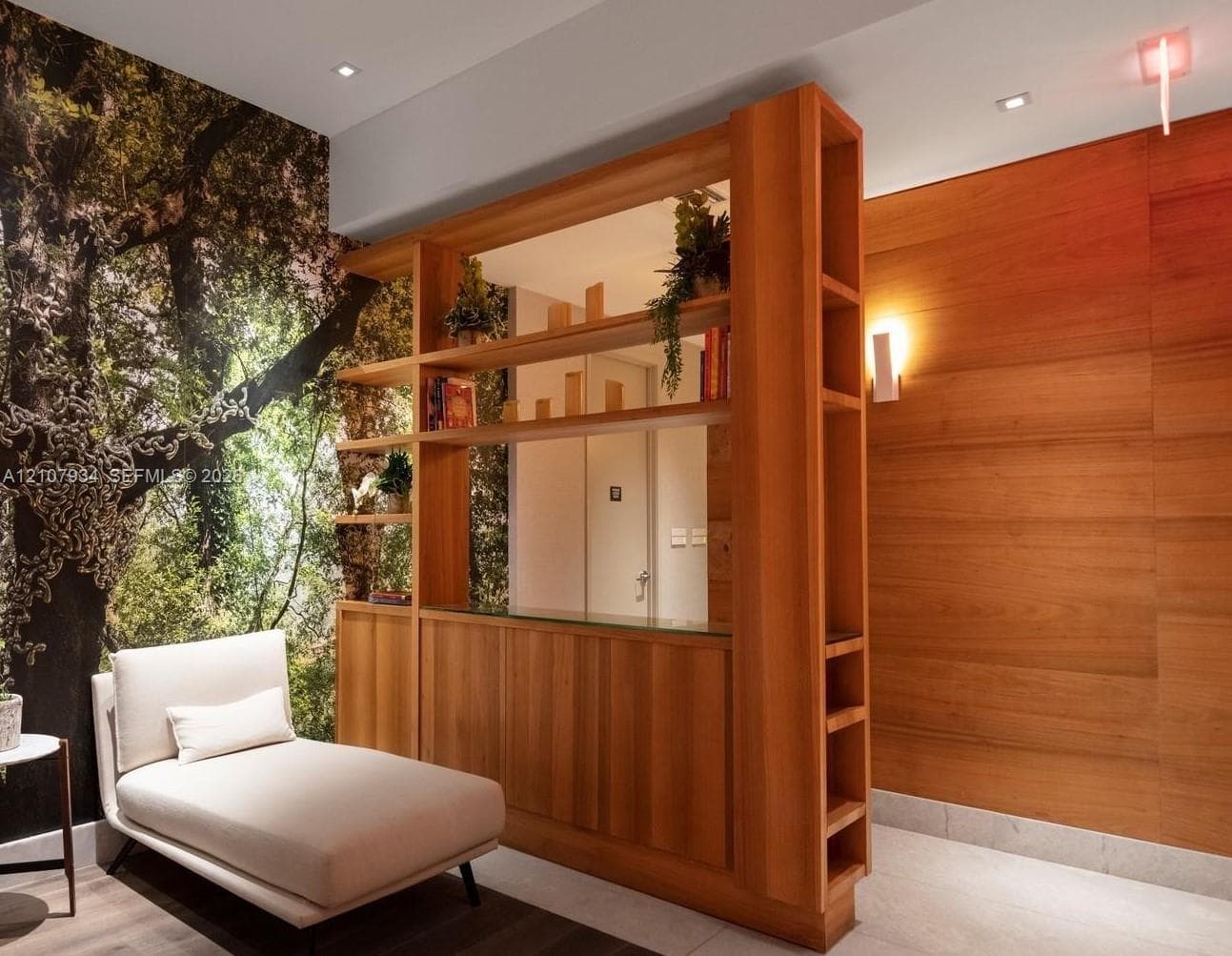 Custom floor-to-ceiling wooden shelving unit with integrated base cabinetry, wood-paneled accent wall, recessed ceiling lighting, and large-scale mural wall covering