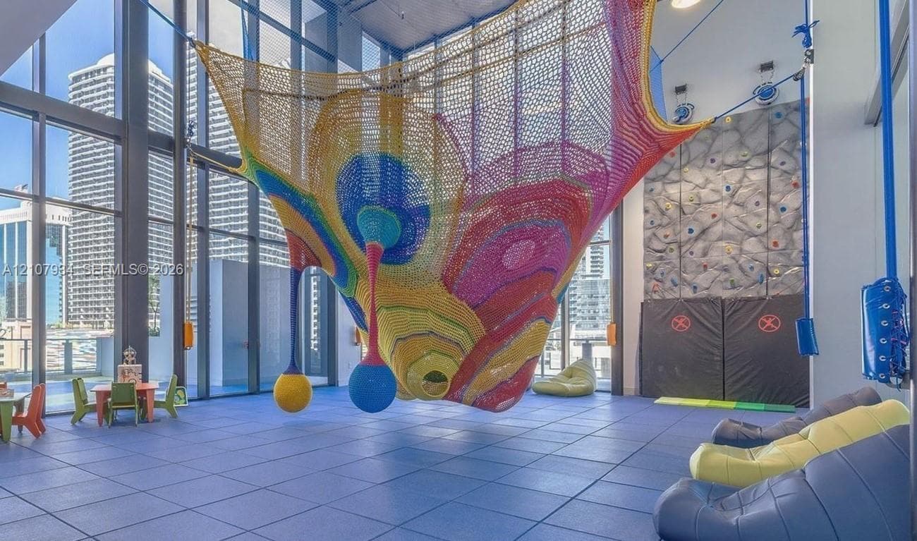 Recreational area featuring floor-to-ceiling windows, integrated rock climbing wall, suspended rope structure, and durable rubberized flooring
