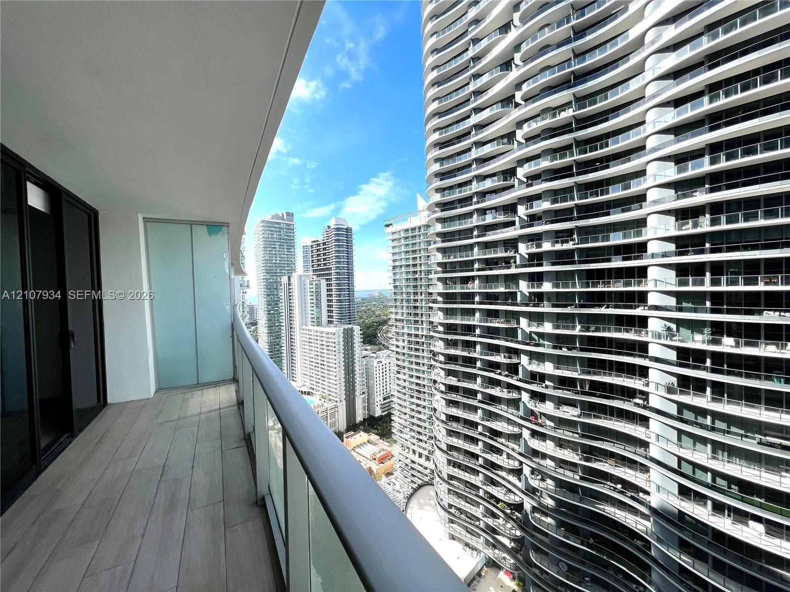 Covered balcony featuring wood-finish flooring, glass panel railings, and floor-to-ceiling sliding glass doors