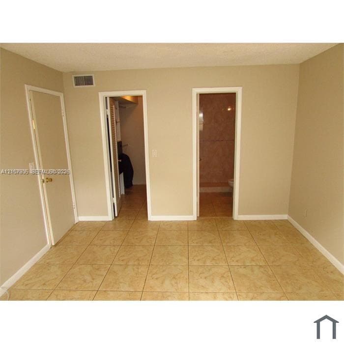 Neutral-toned room featuring large-format ceramic tile flooring, two solid-core interior doors, and built-in closet shelving