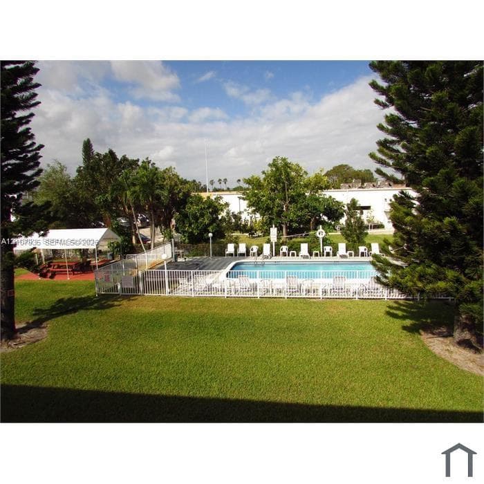 Outdoor swimming pool featuring a perimeter fence, a covered patio area, and mature landscaping within a manicured lawn
