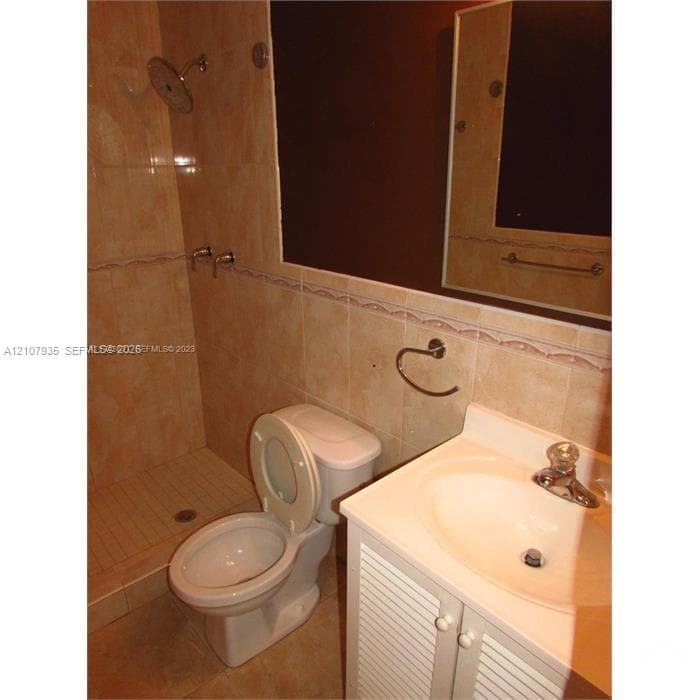 Full-height tiled walk-in shower with integrated wall-mounted showerhead, vanity with integrated basin and polished metal faucet, and large rectangular wall-mounted mirror