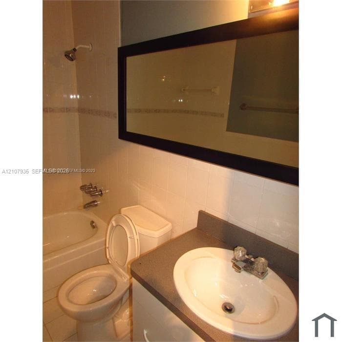 Bathroom featuring a white vanity with a neutral countertop, an integrated sink, a large framed wall mirror, and a tile-surround bathtub with wall-mounted hardware