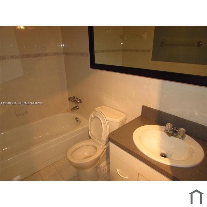 Bathroom featuring a built-in vanity with a stone-finish countertop, undermount sink, porcelain tile flooring, and a recessed bathtub with tile surround