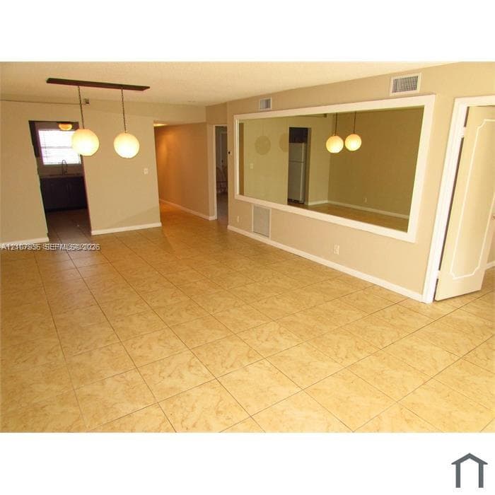 Neutral-toned interior space featuring light-colored square tile flooring, a large wall-mounted mirror with white trim, and a modern two-globe pendant light fixture