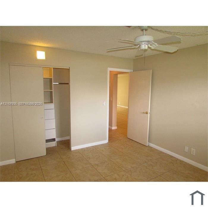 Ceramic tile flooring, white ceiling fan with integrated lighting, and built-in closet cabinetry with shelving and drawers