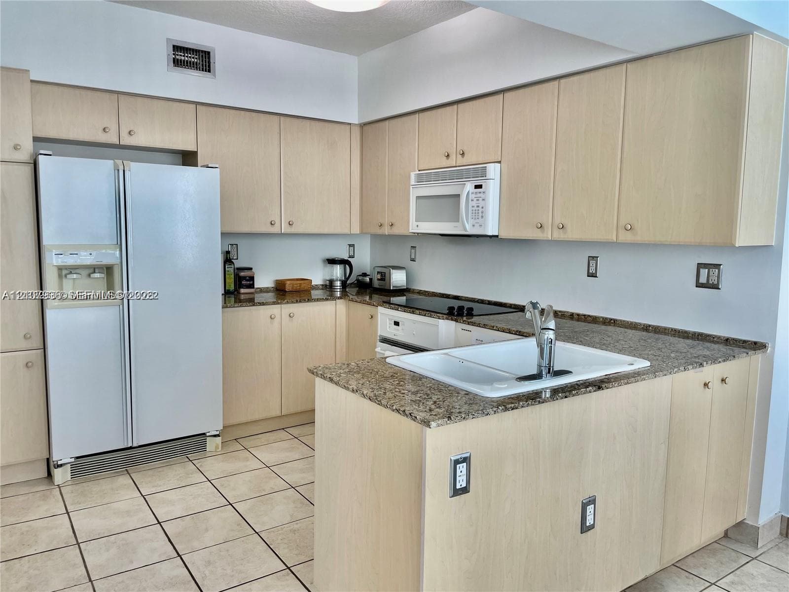 Kitchen featuring light wood-finish cabinetry, stone-surface countertops, a drop-in white sink with a chrome faucet, and tile flooring