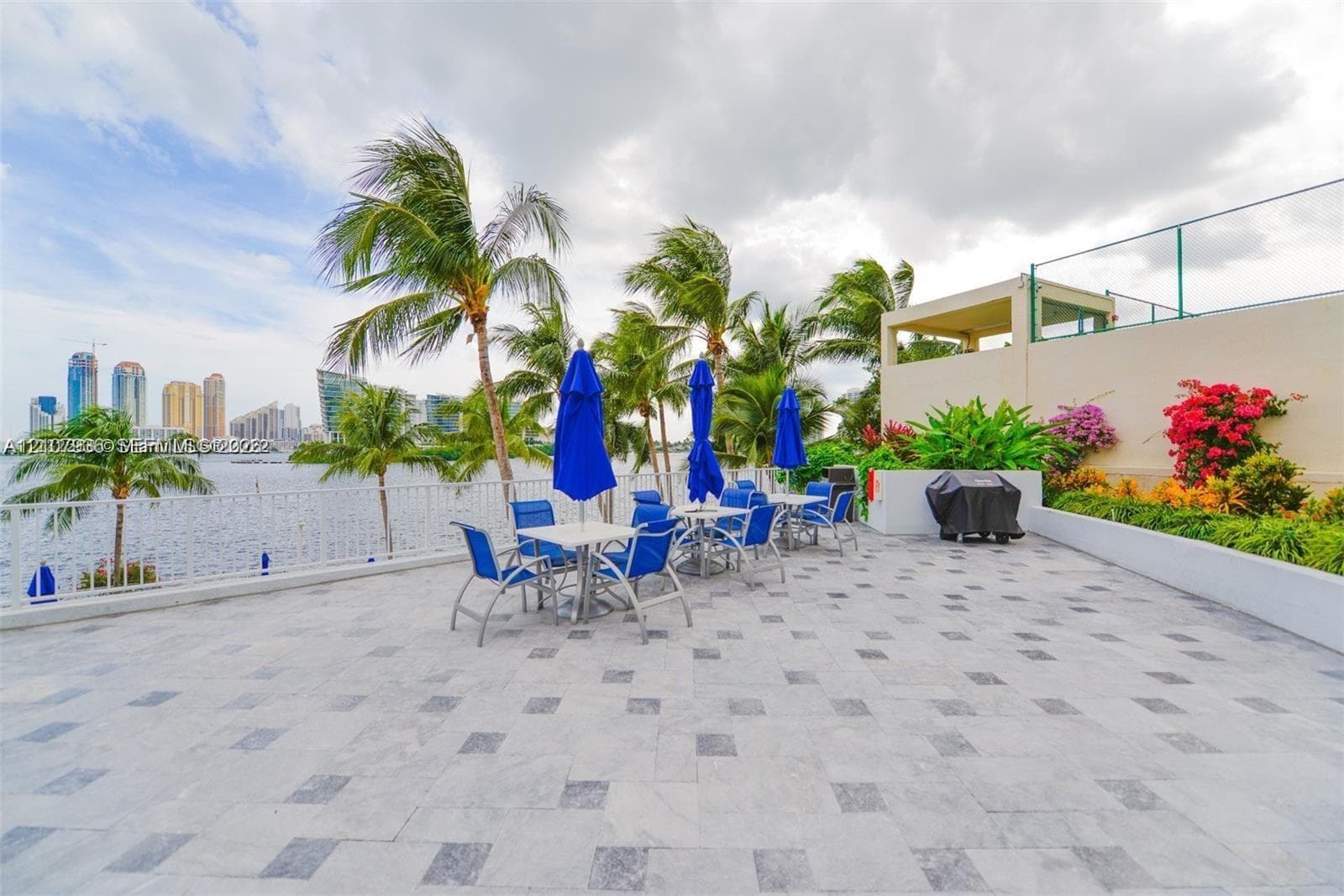 Expansive waterfront terrace featuring patterned stone tiling, decorative perimeter landscaping, and metal railing