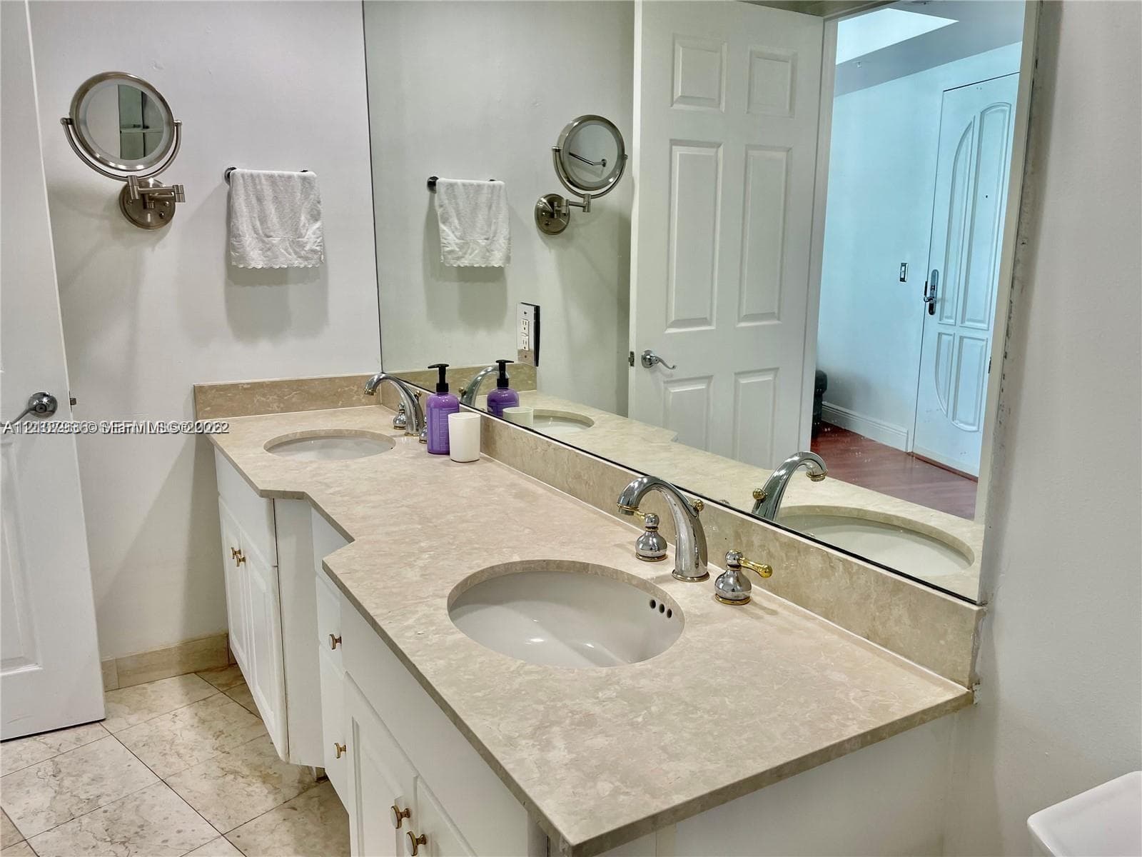 Dual-sink vanity featuring a light-toned solid surface countertop, two undermount basins, chrome-finish widespread faucets, and wall-mounted extendable mirrors