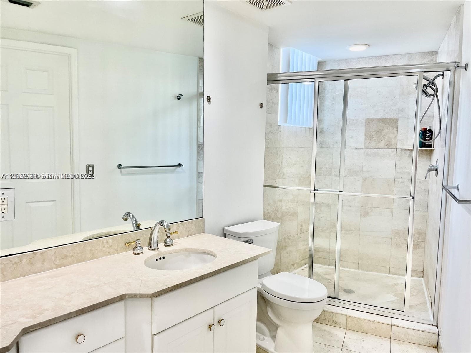 Bathroom featuring a vanity with a stone countertop, an integrated sink, an expansive wall-mounted mirror, a glass-enclosed shower with stone tile surround, and tile flooring