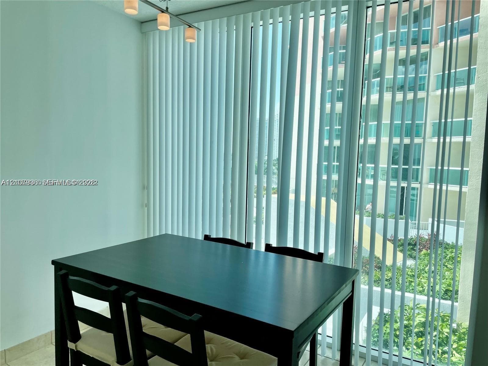 Floor-to-ceiling windows featuring vertical blinds, neutral tile flooring, and a three-light bar pendant fixture