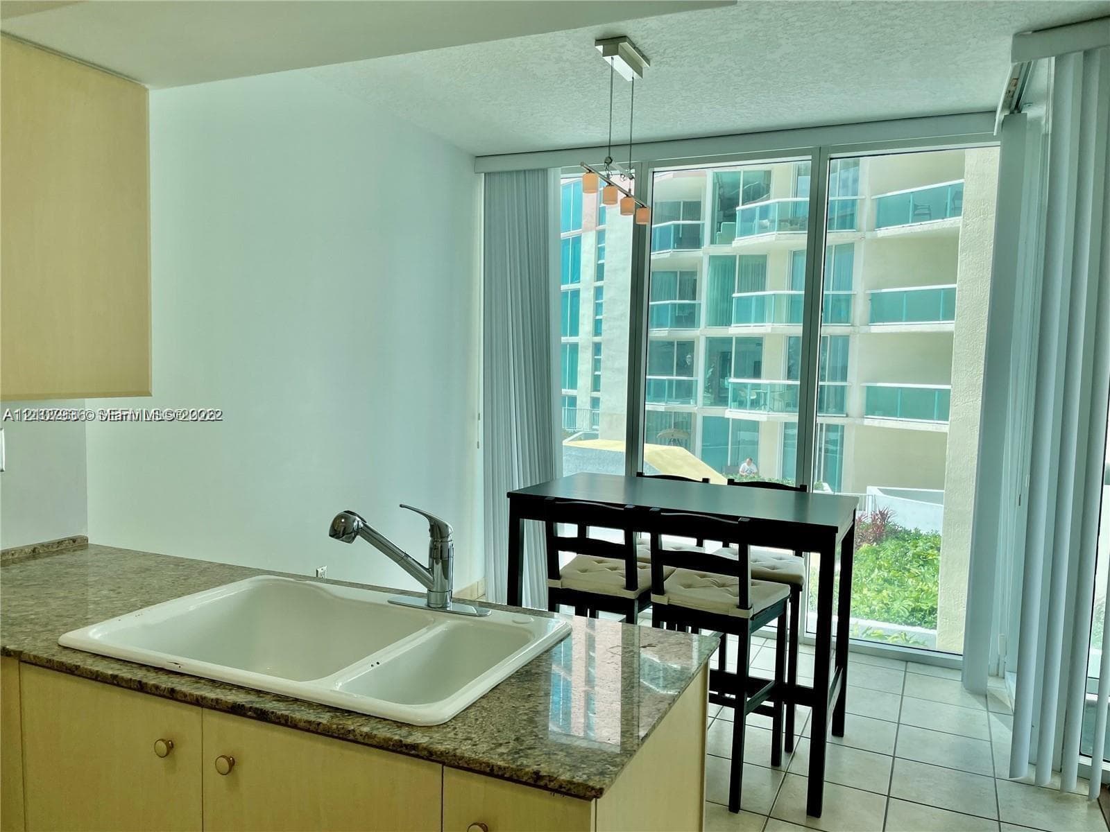 Kitchen featuring stone-composite countertops, dual-basin sink, high-arc faucet, tile flooring, and floor-to-ceiling glass paneling