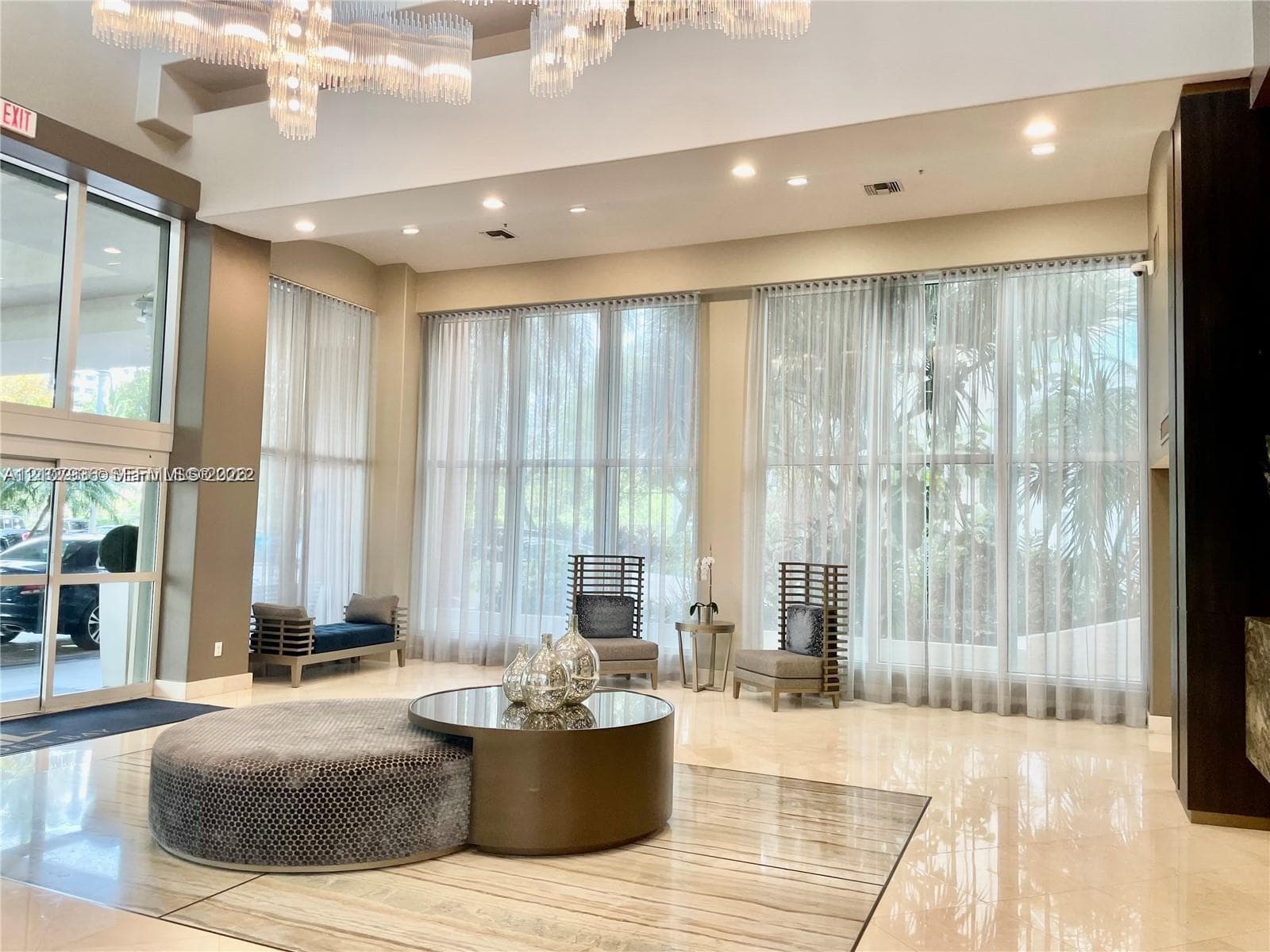 Grand foyer featuring high ceilings, large-format stone tile flooring, expansive floor-to-ceiling windows, and a decorative chandelier