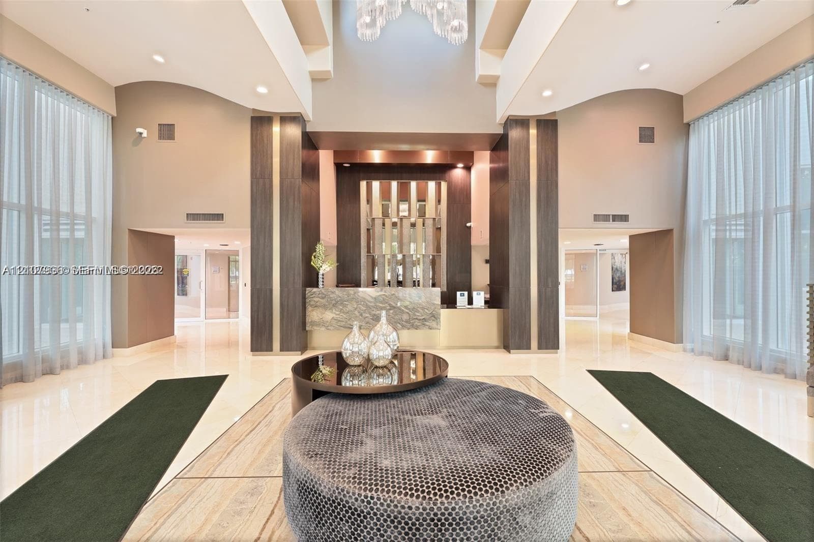 Double-height ceiling, floor-to-ceiling windows, polished stone flooring, custom architectural columns, and a stone-clad reception desk