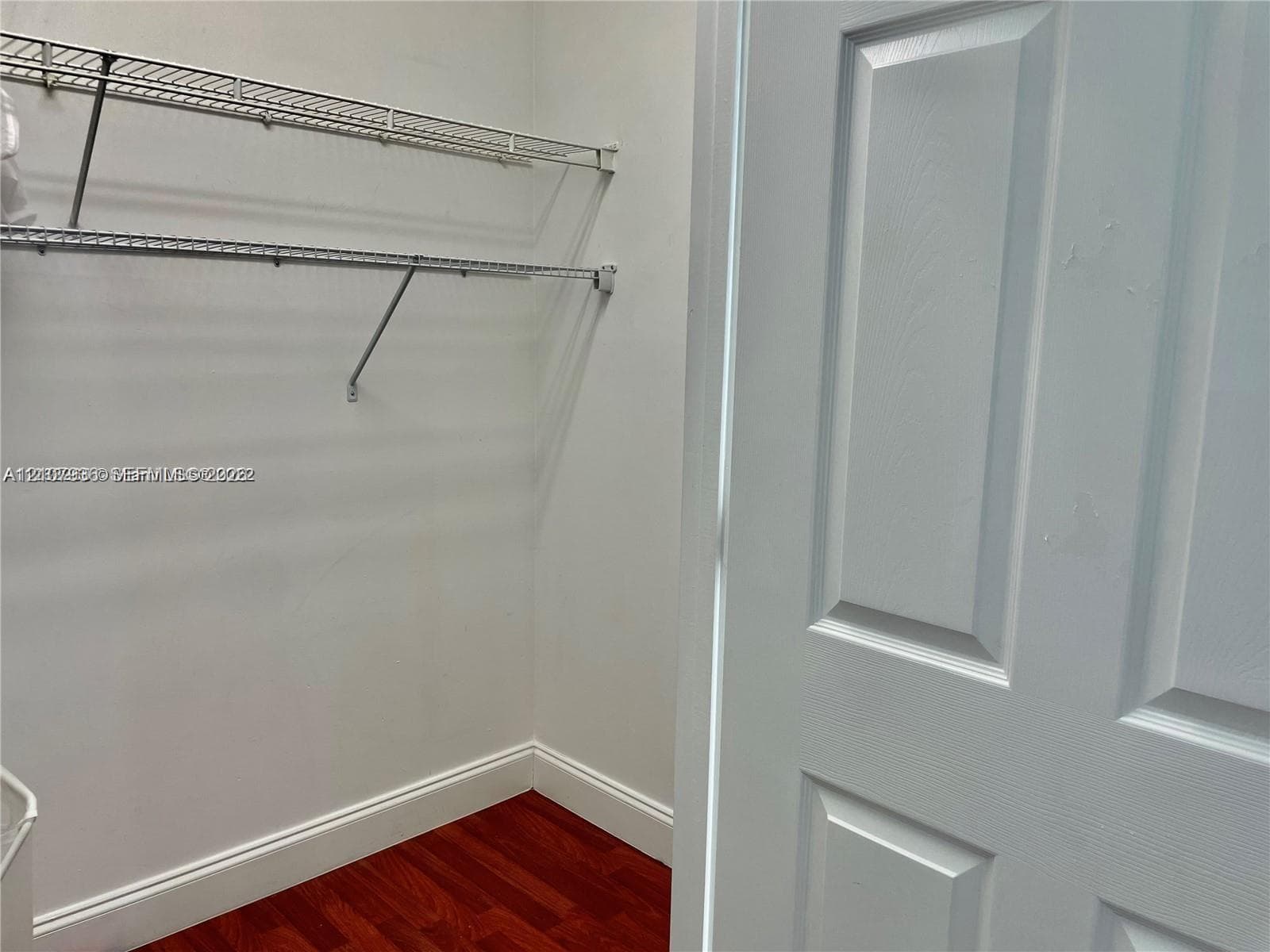 Storage area featuring white paneled door, wood-finish flooring, and tiered wire shelving