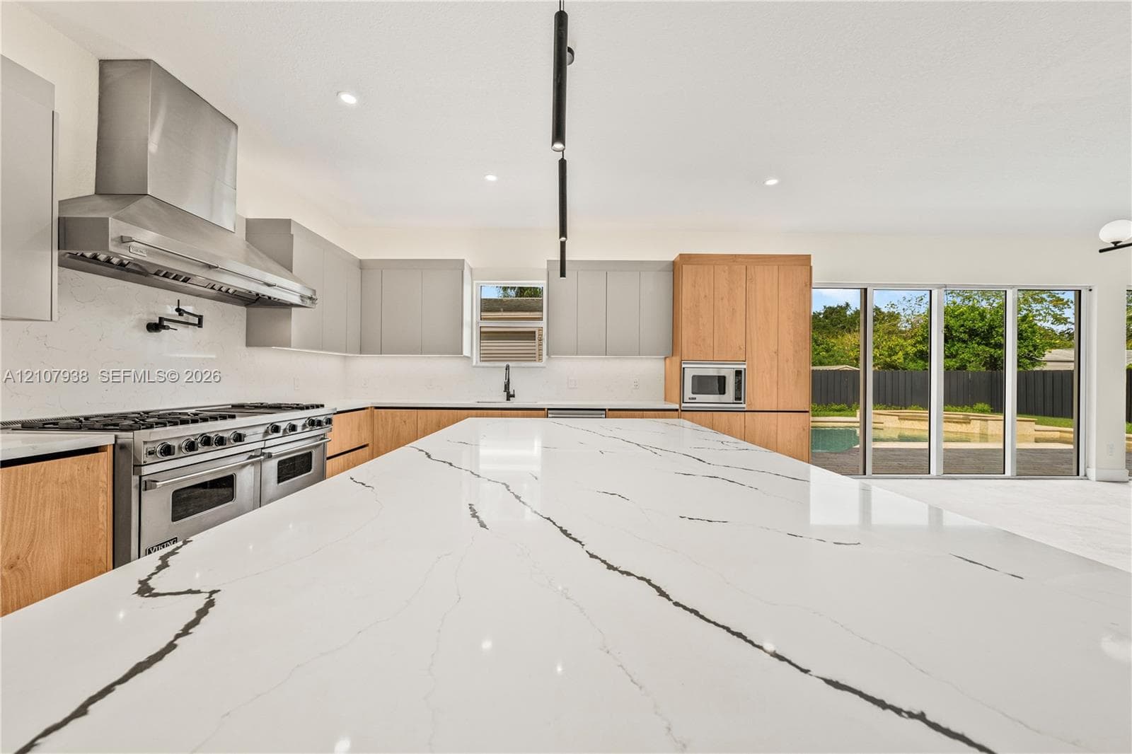 Kitchen featuring an expansive center island with waterfall-edge stone countertops, stainless steel professional-grade range, stainless steel chimney-style range hood, two-tone flat-panel cabinetry, and floor-to-ceiling sliding glass doors