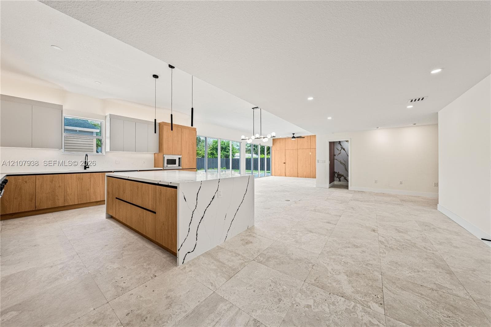 Kitchen featuring a large waterfall-edge stone island, two-tone cabinetry, stone flooring, integrated overhead lighting, and multi-panel glass doors