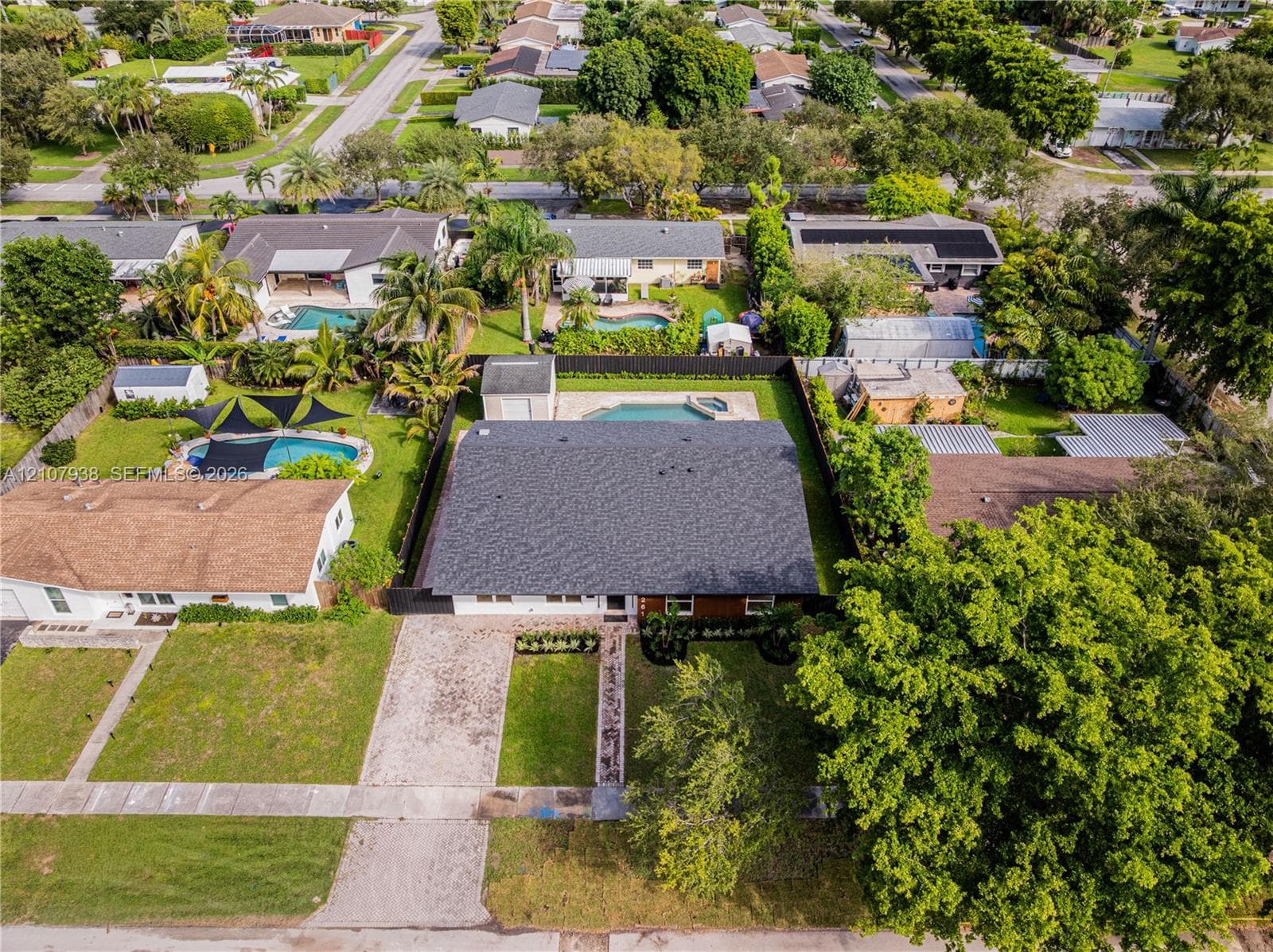 Aerial perspective featuring an asphalt shingle roof, paved driveway, detached storage structure, and a fenced backyard with an in-ground swimming pool
