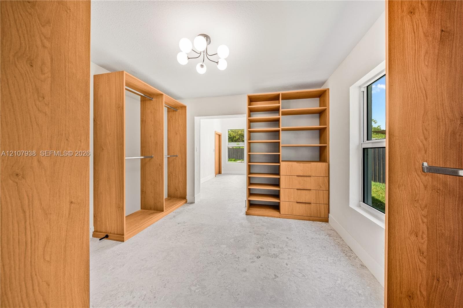 Custom walk-in closet featuring extensive wood-finish built-in cabinetry, integrated shelving, multi-drawer storage, and a modern multi-bulb flush-mount light fixture