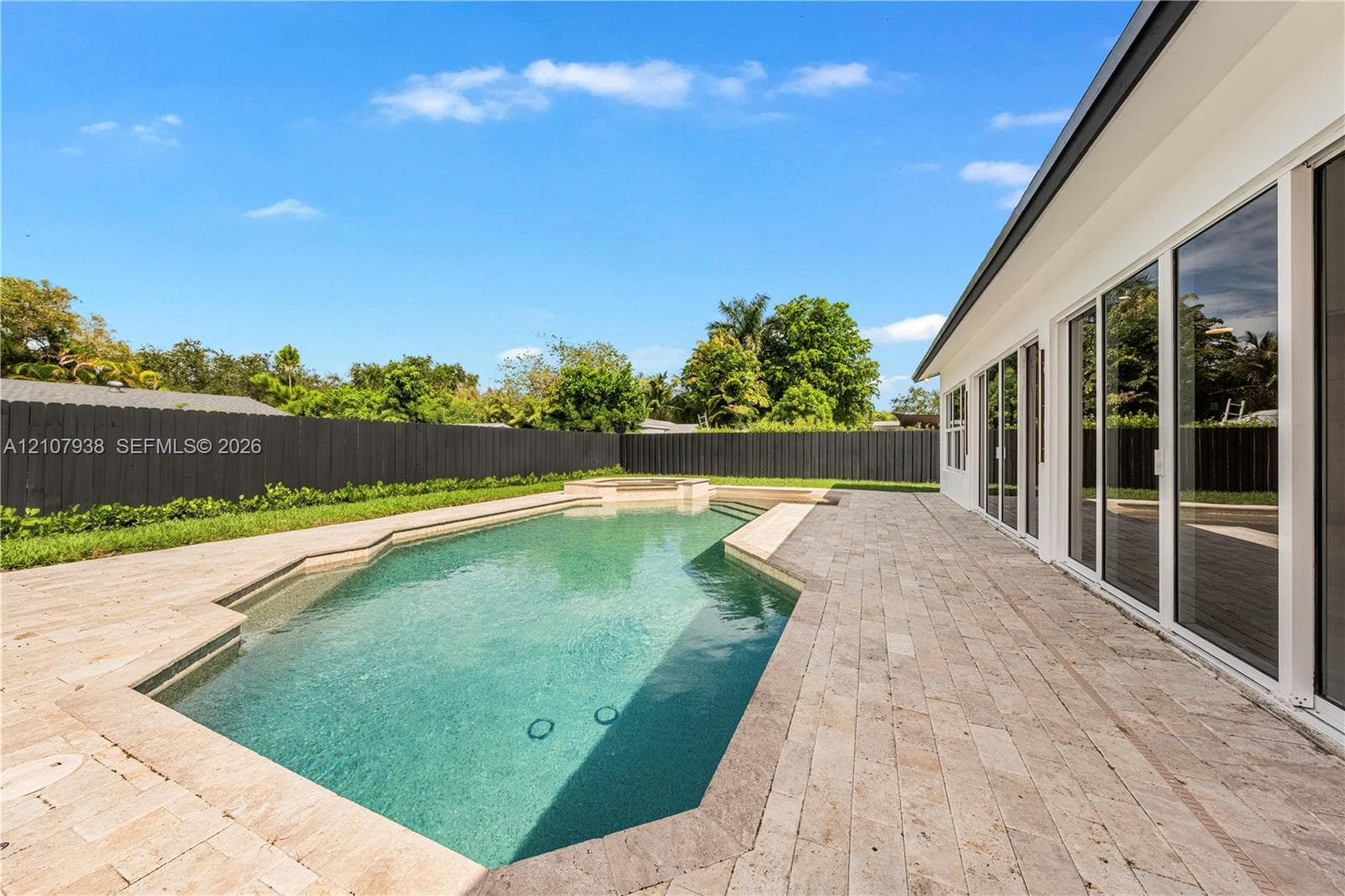 Outdoor space featuring a geometric inground pool, integrated spa, expansive stone paver decking, and privacy fencing