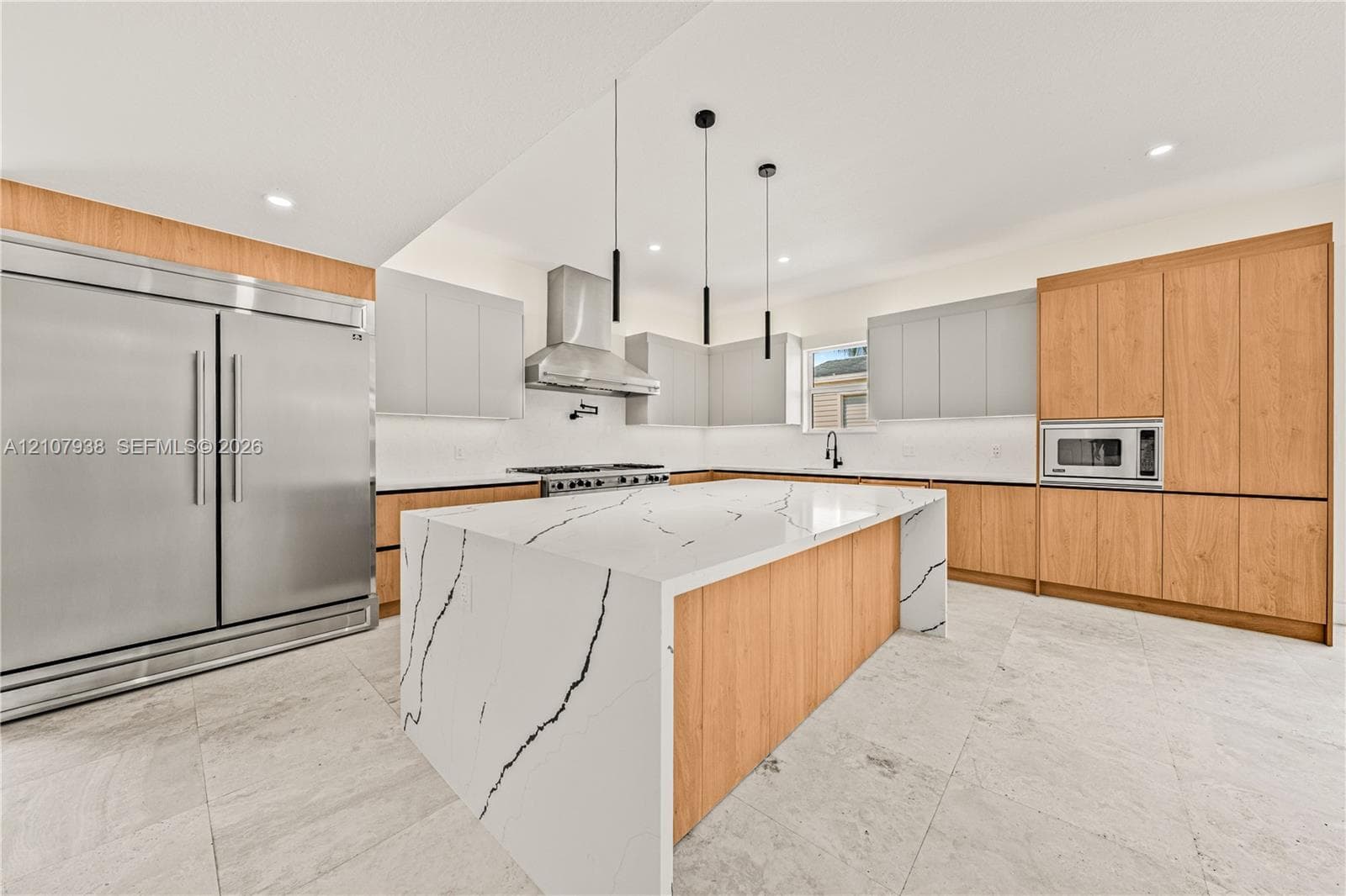 Kitchen featuring a large island with a stone-finish waterfall countertop, wood-finish cabinetry, stainless steel professional-grade appliances, under-cabinet lighting, and stone flooring