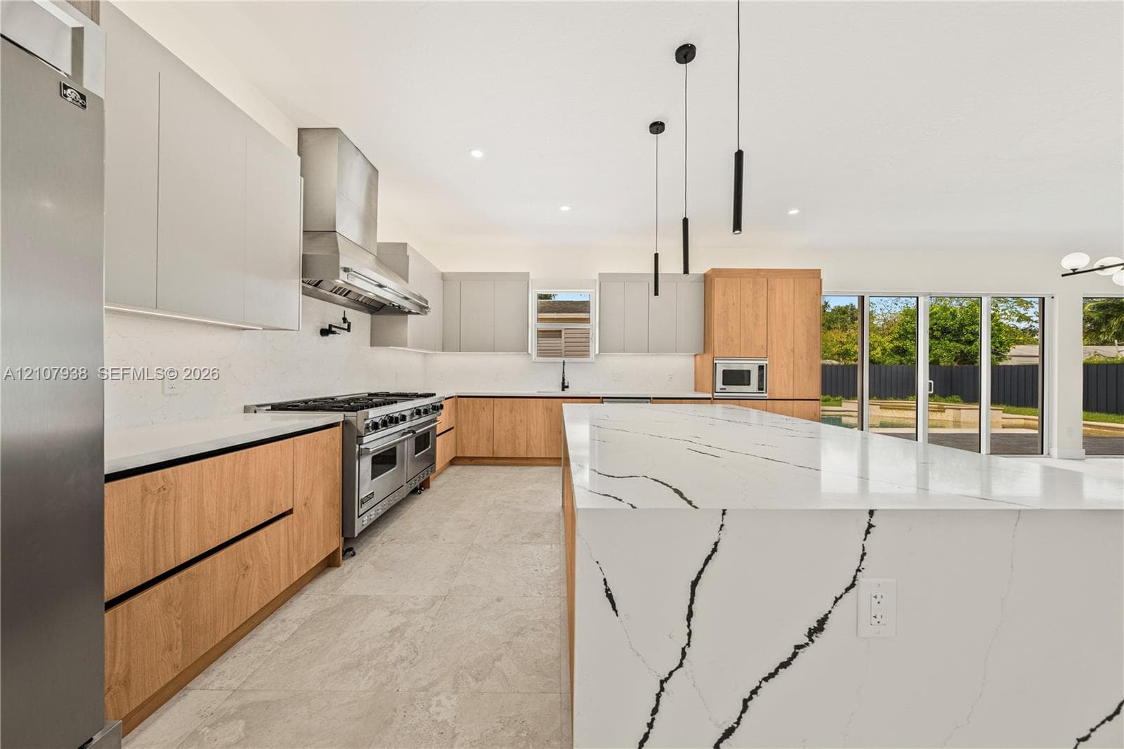 Kitchen featuring a large waterfall island with veined stone countertops, two-tone flat-panel cabinetry, a professional-grade stainless steel range, and minimalist pendant lighting