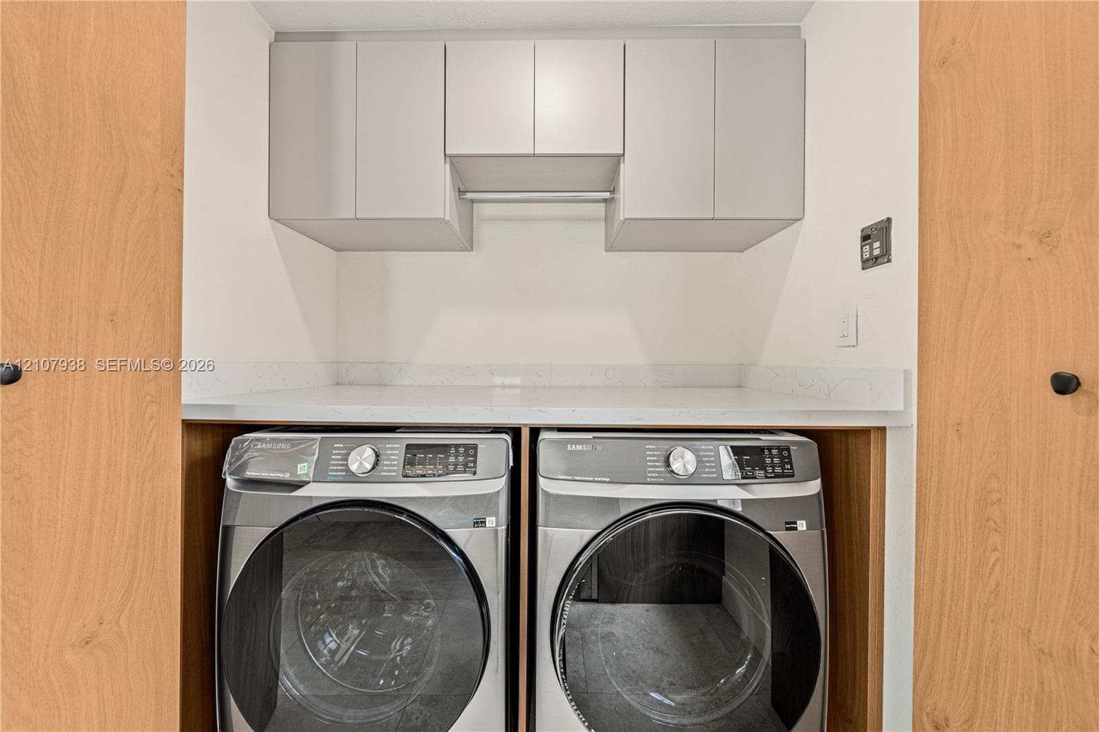 Laundry area featuring overhead cabinetry, solid-surface countertop, and wood-finish cabinetry doors