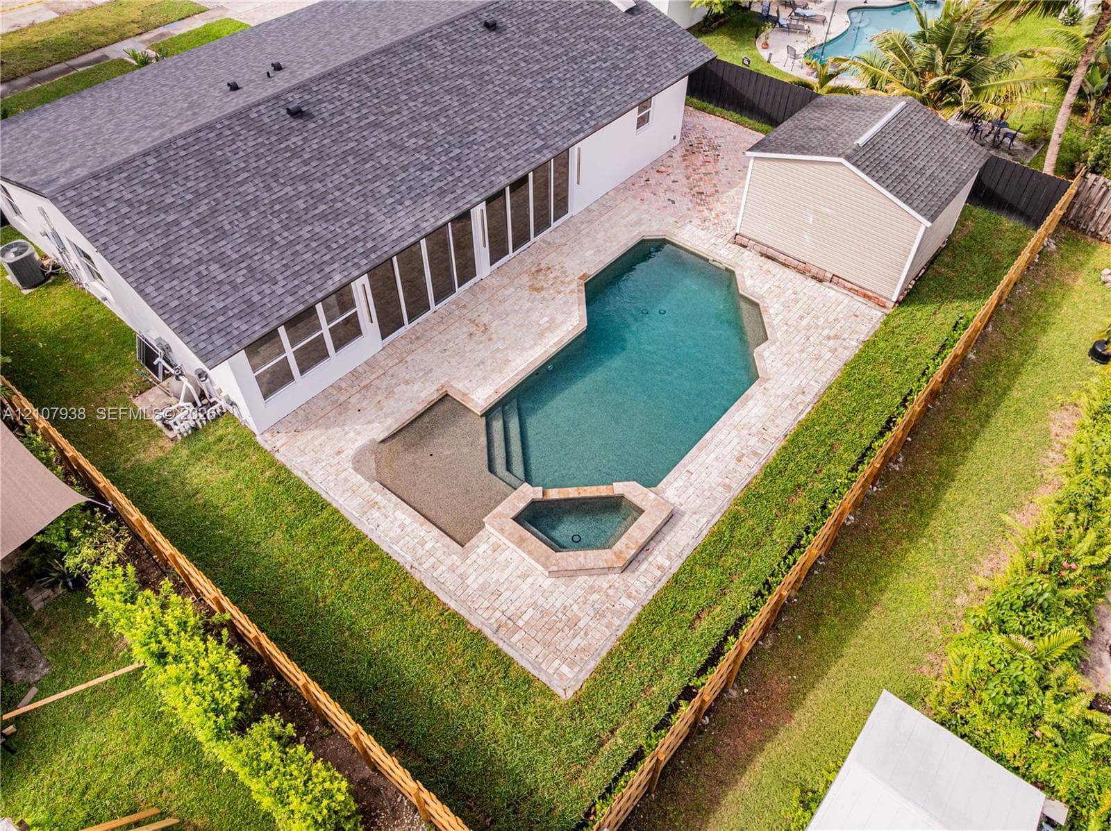 Backyard featuring an in-ground pool with an integrated spa, stone-paver decking, a detached storage shed, and a fully fenced perimeter