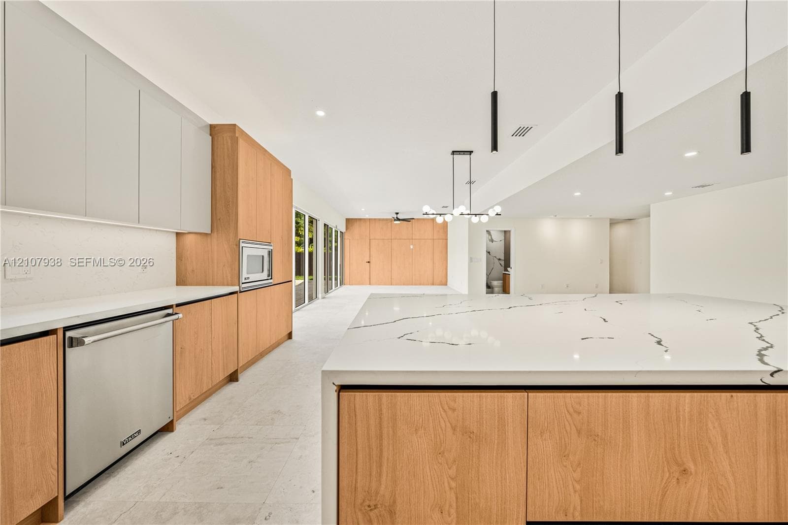 Modern kitchen featuring a large central island with waterfall-edge countertop, dual-tone cabinetry, stainless steel built-in appliance, and contemporary pendant lighting
