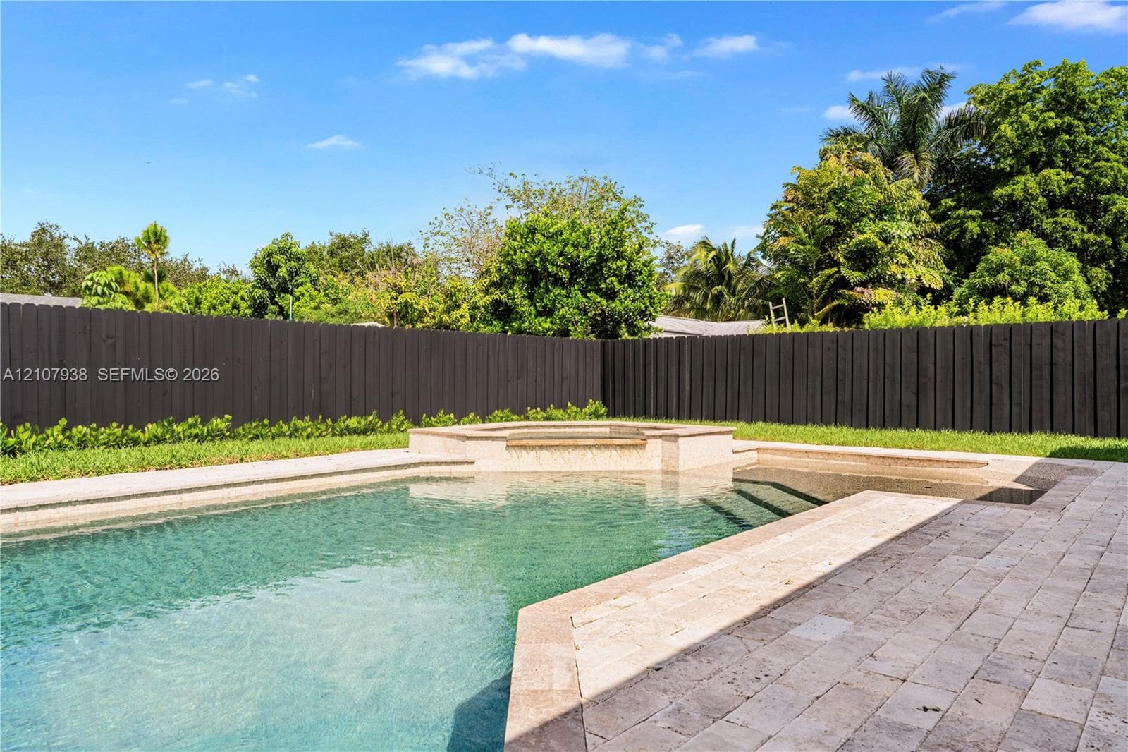 In-ground swimming pool with integrated spa, stone-paver decking, and perimeter wood fencing