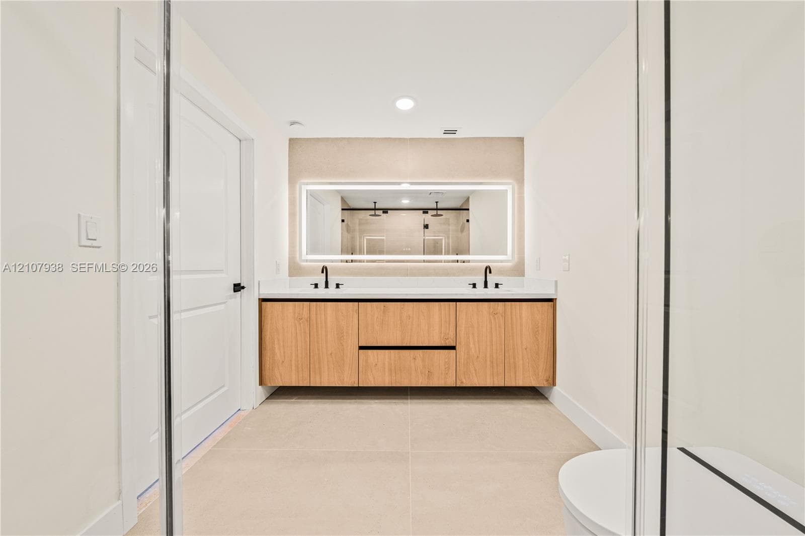 Floating wood-finish double vanity with stone countertop, dual undermount sinks, matte black widespread faucets, and a large integrated LED-backlit mirror