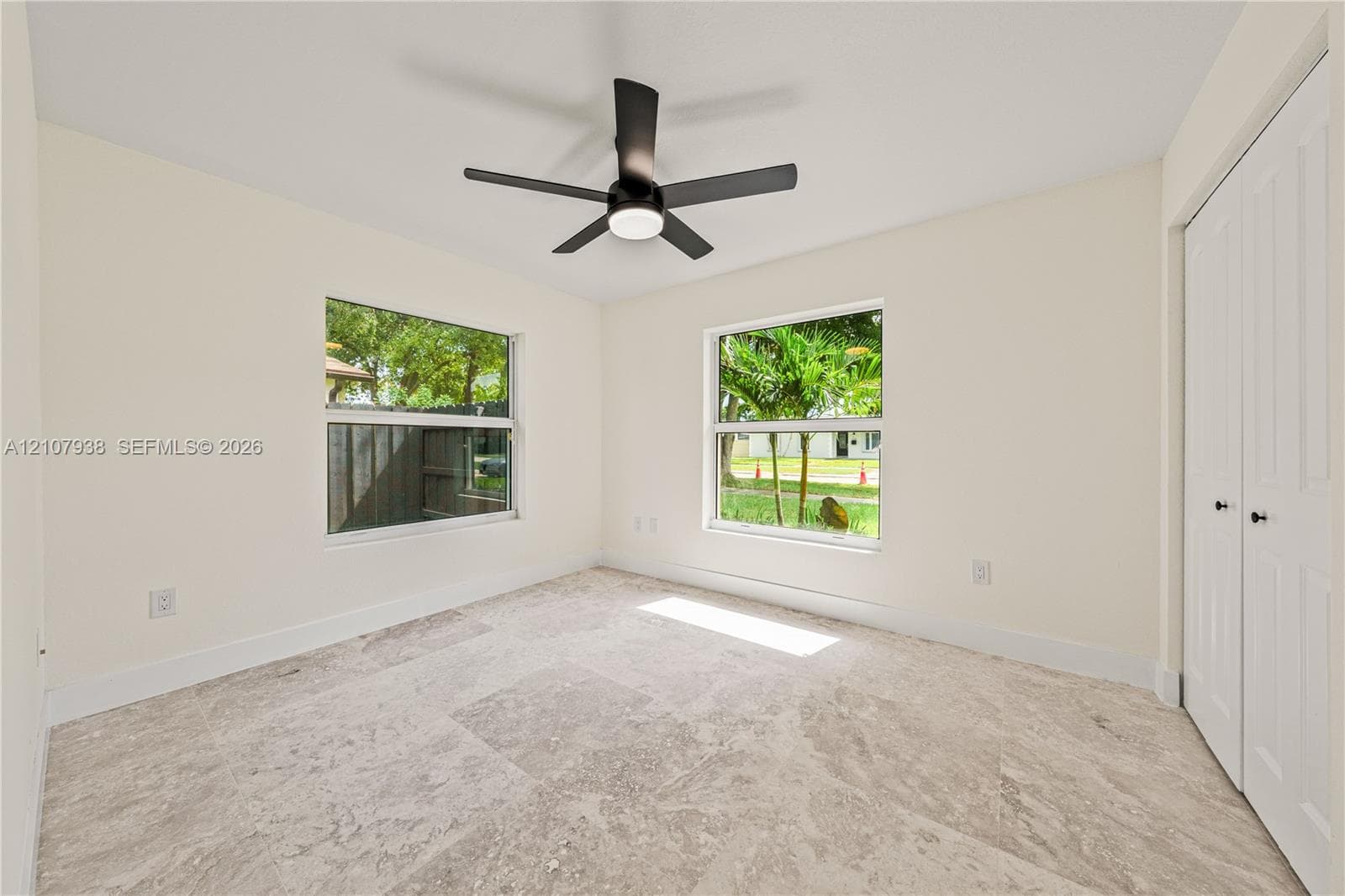 Neutral-toned tile flooring, dual windows with natural light, a ceiling-mounted fan with integrated lighting, and white bi-fold closet doors