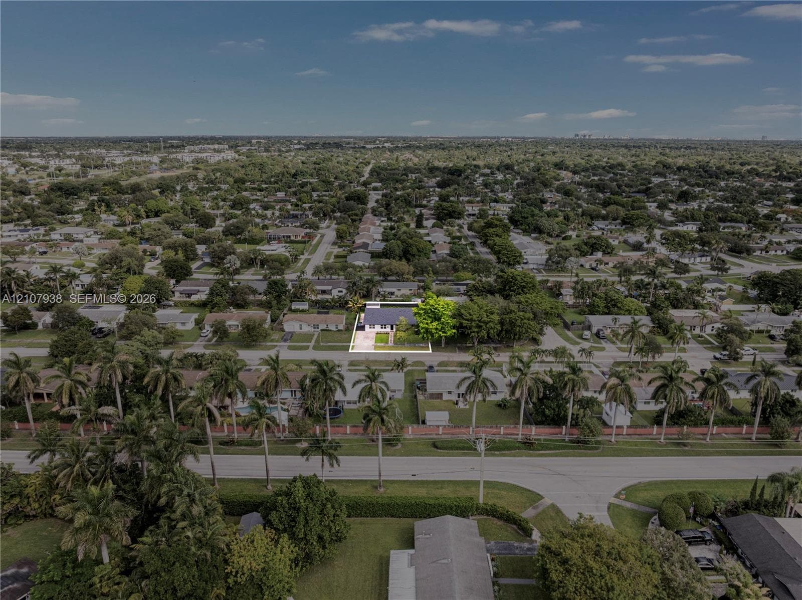 Aerial perspective of a detached residence featuring a paved driveway, a large mature shade tree, and a grass lawn on a rectangular lot