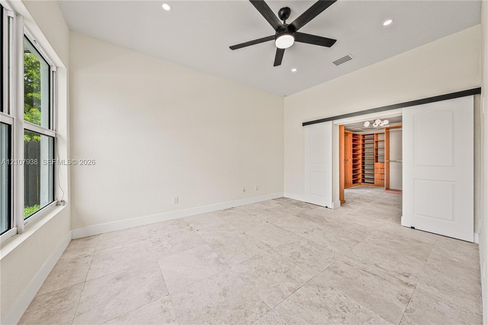 Large-format tile flooring, ceiling-mounted matte black fan, recessed lighting, and dual white sliding barn doors revealing built-in storage cabinetry