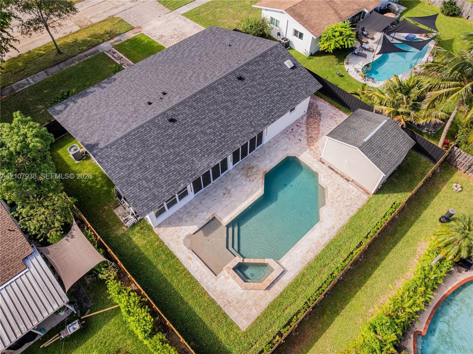 Rear exterior featuring a paver patio, in-ground swimming pool, integrated spa, and a detached storage structure enclosed by perimeter fencing