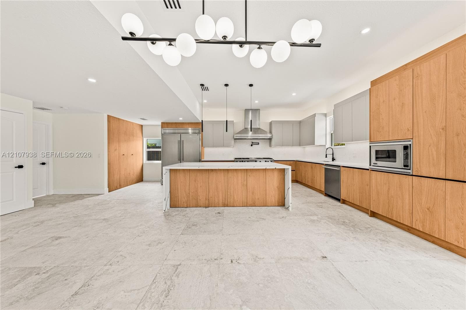 Kitchen featuring a central island with a stone-finish countertop, two-tone cabinetry with wood-finish and matte-finish panels, stainless steel appliances, and multi-light pendant fixtures