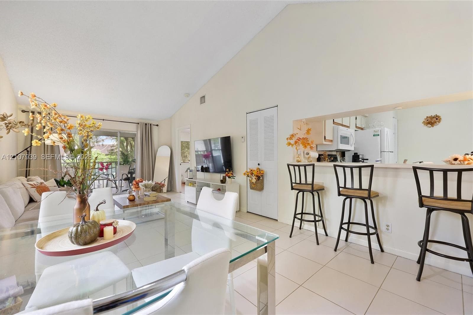 Vaulted ceiling, open-concept floor plan, tile flooring, and kitchen passthrough window with breakfast bar