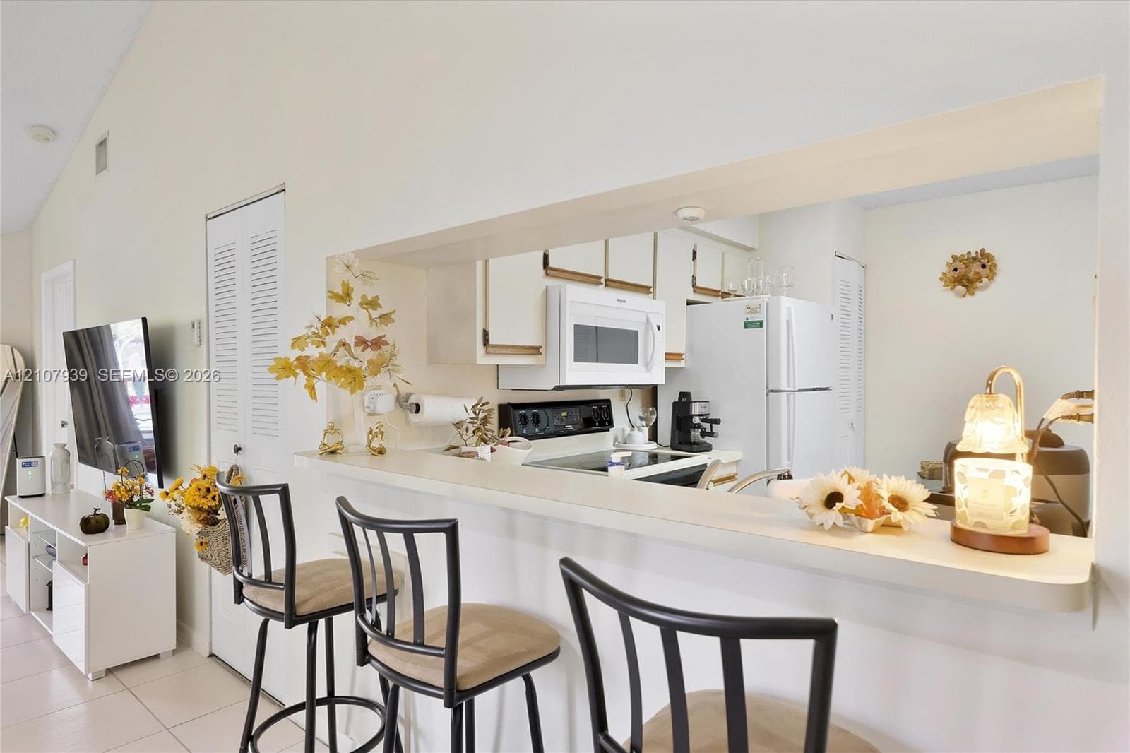 Kitchen featuring a breakfast bar with a solid surface countertop, white cabinetry, a built-in microwave, and a white refrigerator