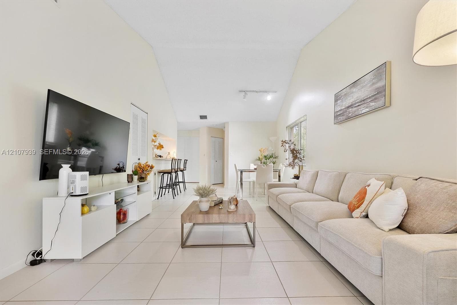 Open-concept living area featuring vaulted ceilings, light-toned ceramic tile flooring, and a built-in breakfast bar