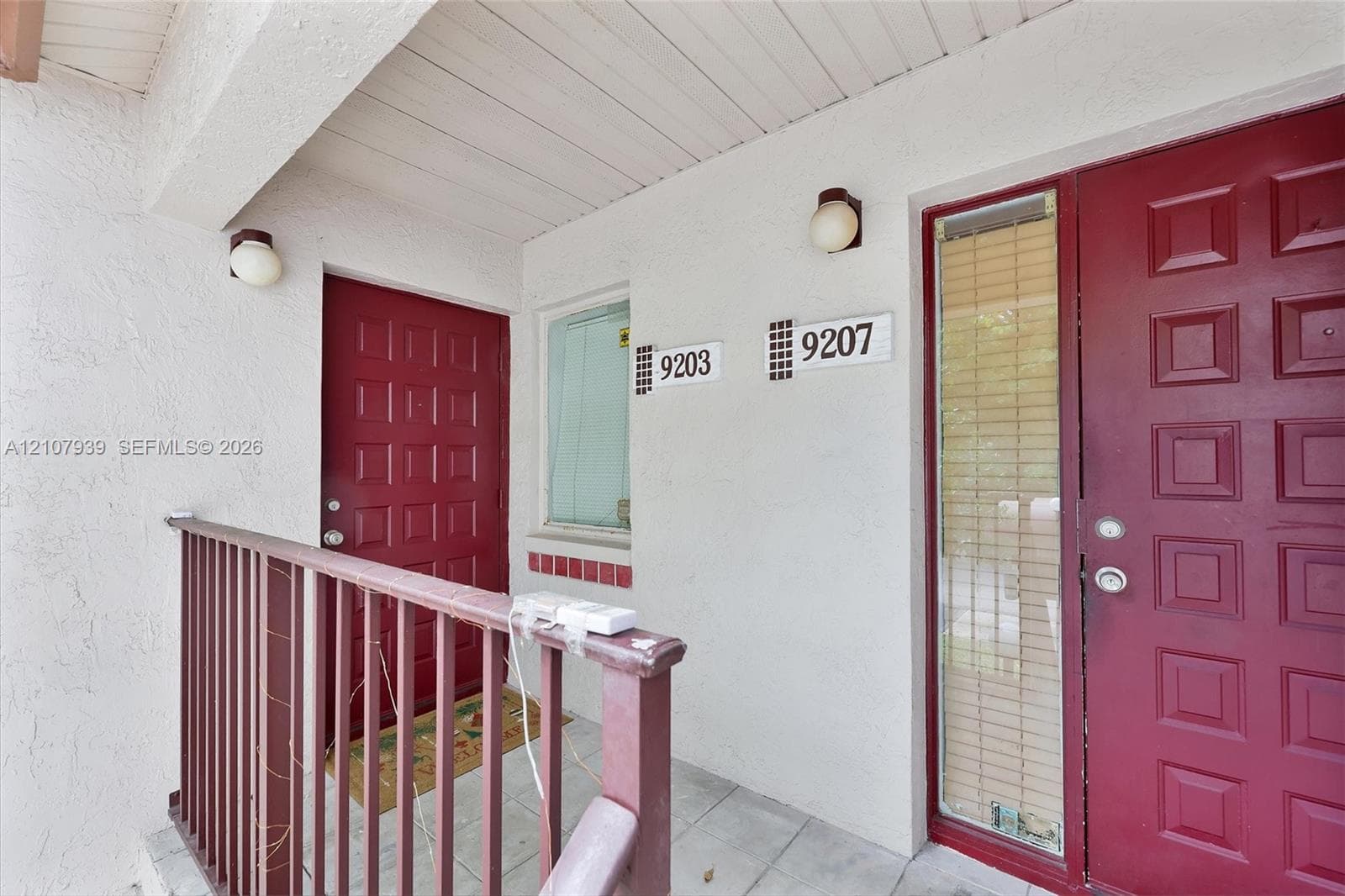 Covered entryway featuring dual paneled entry doors, textured exterior walls, tiled flooring, and matching metal railing