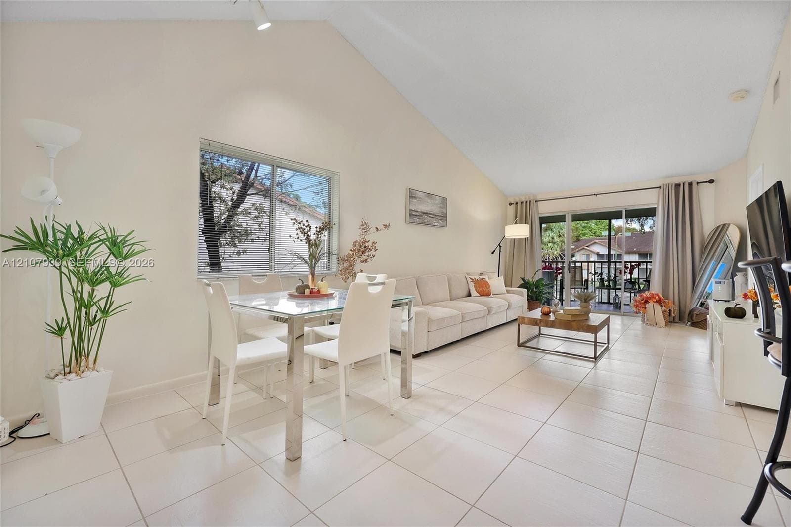 Vaulted ceilings, large-format tile flooring, oversized window, and sliding glass door leading to a private balcony