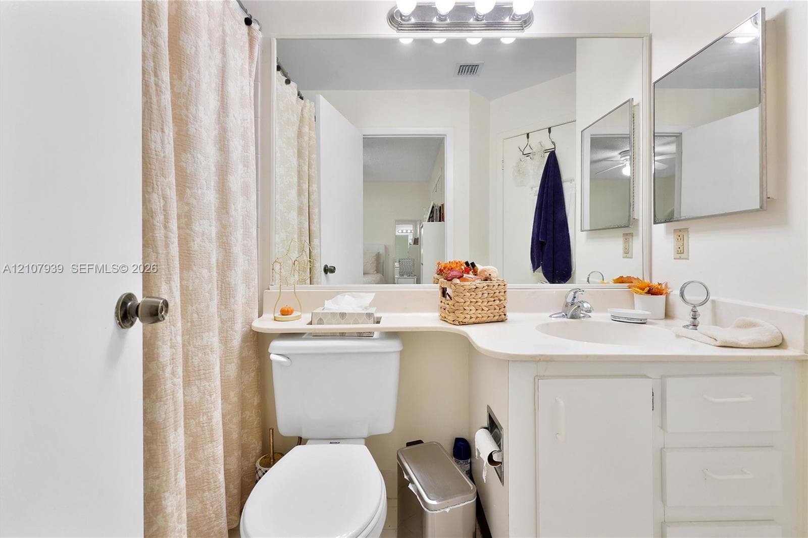 Bathroom featuring a vanity with integrated countertop and sink, large wall-to-wall mirror, multi-bulb overhead lighting, and built-in cabinet storage