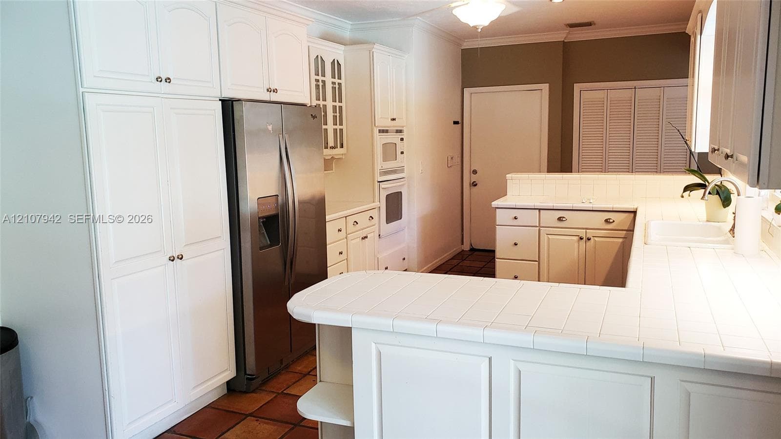 Kitchen featuring white cabinetry with glass-panel accents, tile countertops, stainless steel side-by-side refrigerator, built-in wall oven, and tile flooring