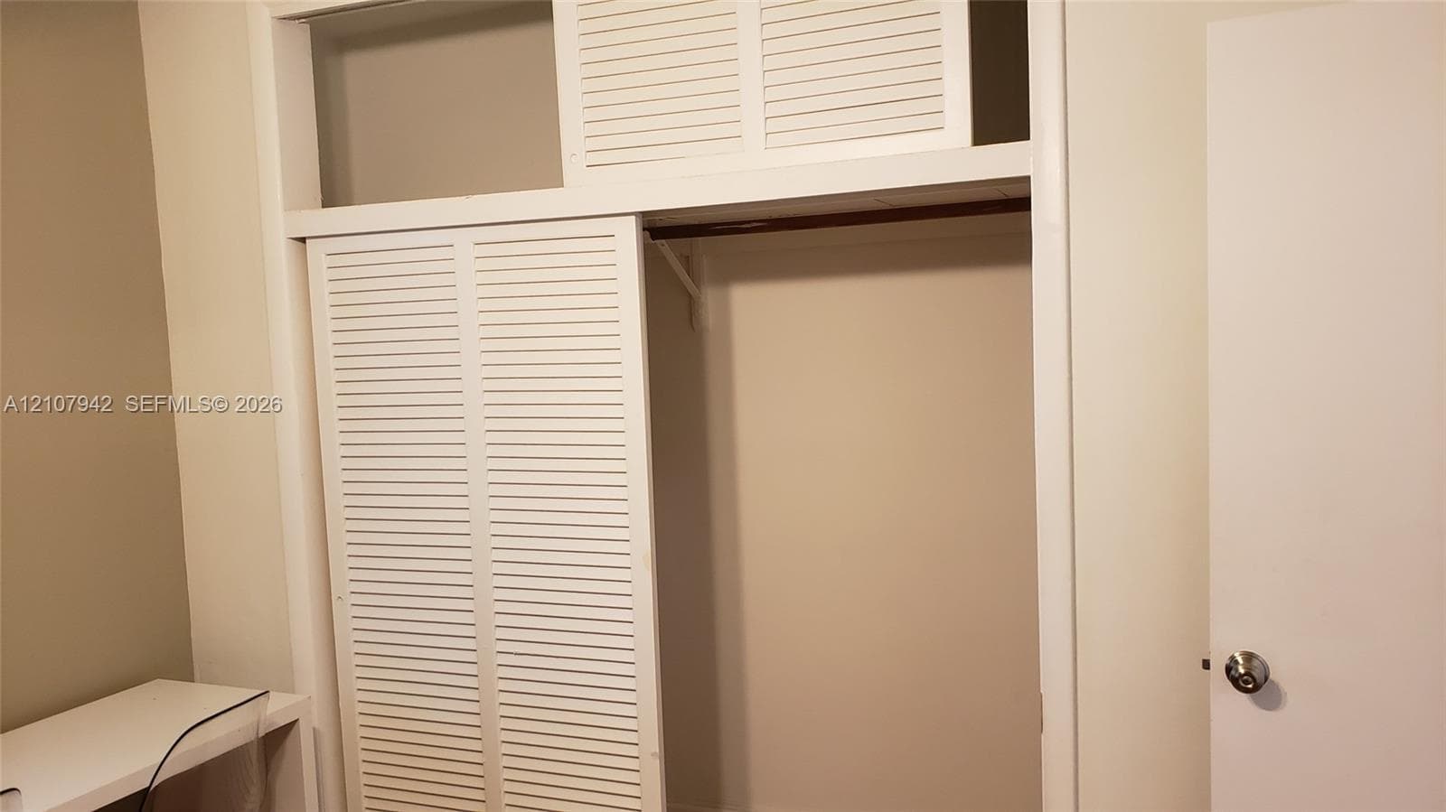 Storage closet featuring white louvered sliding doors, upper transom storage panels, and a built-in hanging rod