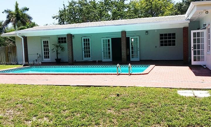 Exterior features include a covered patio with brick columns, a rectangular inground pool, red brick pool decking, and multiple sets of glass-paned doors