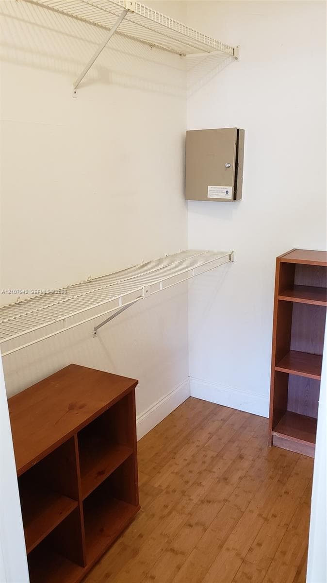 Storage space featuring wall-mounted wire shelving, wood-finish flooring, and built-in vertical shelving units