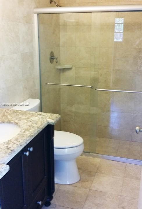 Bathroom featuring a vanity with stone countertop, drop-in sink, glass-enclosed shower, and stone-finish floor and wall tile