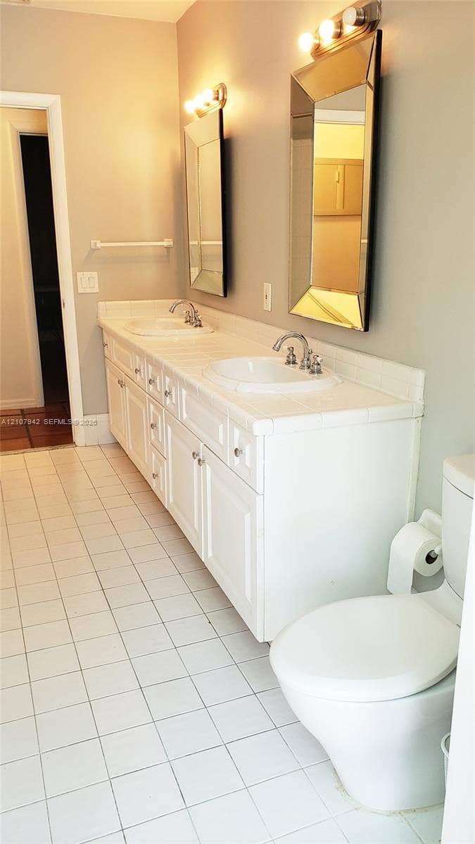 Dual-sink vanity with white cabinetry and countertop, integrated basin sinks, dual wall-mounted mirrors, and white tile flooring
