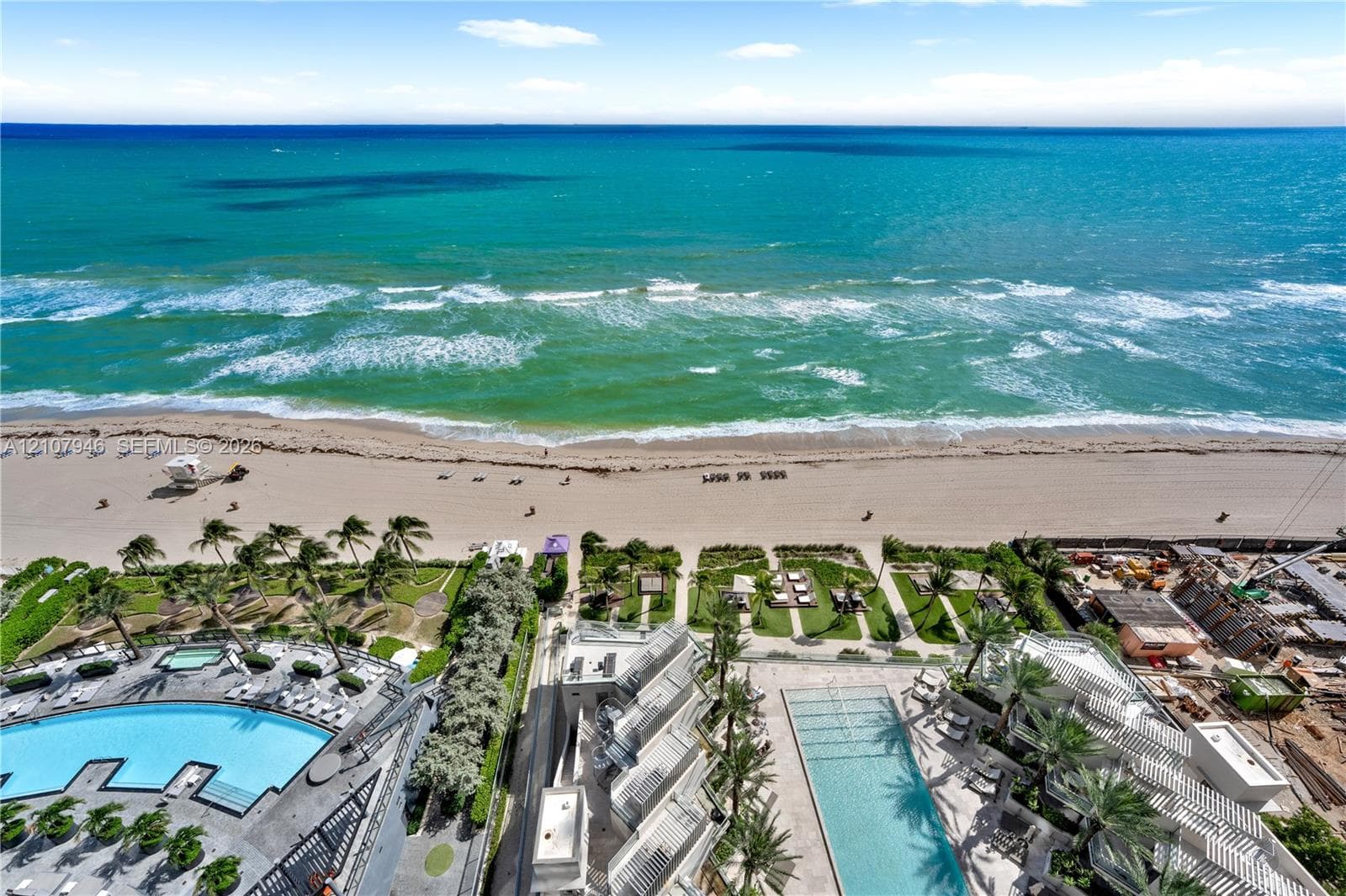 Direct oceanfront location with expansive sandy beach access, featuring multi-level swimming pools, manicured palm landscaping, and paved sun decks